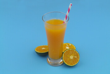 Orange juice glass with drink straw and orange fruits on blue background	