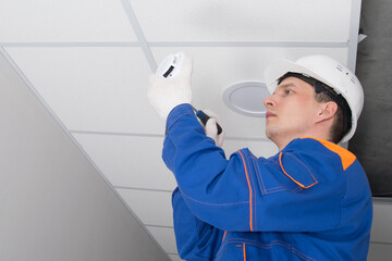 a master in a protective helmet for the maintenance of fire alarms, conducts an inspection in the residential sector