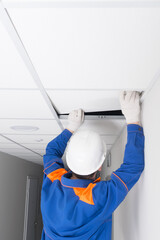 a master in a protective helmet, for the installation of suspended ceilings, completes the assembly of plates, rear view