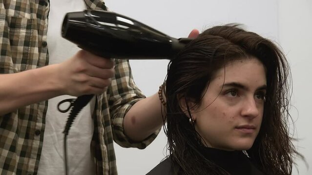 Young woman's thick dark hair blow dried by male stylist in salon
