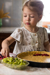 portrait of little cheerful girl helping her mother to cook and decorate a pie fruits and berries on a wooden table in the kitchen with natural light coming through a window