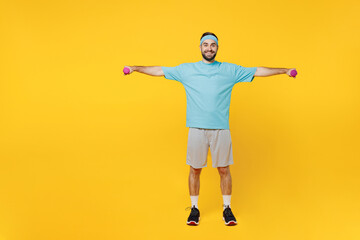 Fototapeta na wymiar Full body young fitness trainer instructor sporty man sportsman in headband blue t-shirt spend weekend in home gym hold dumbbells isolated on plain yellow background Workout sport motivation concept.