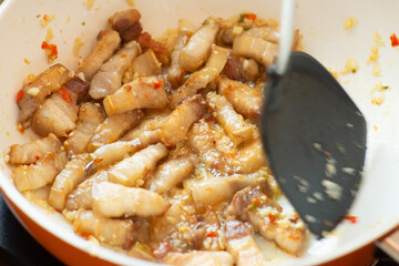 cooking spicy belly prok slice on white plate electric pan and black turner