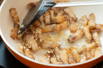 cooking spicy belly prok slice on white plate electric pan and black turner