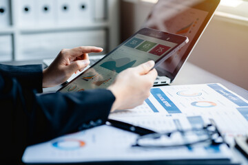 Close up of Businesswomen or Accountant using a digital tablet and laptop computer analytic business report graph and finance chart at the workplace, financial and investment concept.