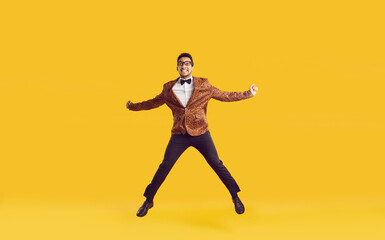 Fototapeta na wymiar Happy dark skinned showman dressed in stylish chic having fun and celebrating his achievements. Attractive young guy in leopard jacket funny jumps isolated on yellow background. Banner. Full length.