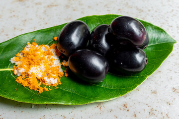 Spicy mixed salt with some black java plum fruit in the green leaves. A way to eat ripe cesium camini fruit by hand. 4k closeup video.
