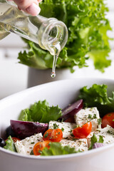 Woman pouring olive oil in a bowl of greek salad