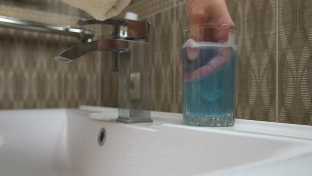 Close-up of washing a polymer aligner in a glass of cleaning solution of water. The hands of a Caucasian woman take out an aligner for correcting an overbite from a glass