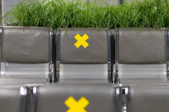 Metal Seat Section At The Airport With A Yellow Cross Sticker. Empty Seating On The Waiting Bench.Public Spaces During The Pandemic.A Call For Social Distancing.Journey Into The Pandemic