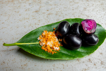 Spicy mixed salt with some black java plum fruit in the green leaves. A way to eat ripe cesium camini fruit by hand. 4k closeup video.