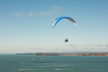 A hang-glider soars through the air over Auckland's Hauraki Gulf on a sunny day. Blue skies, boats...