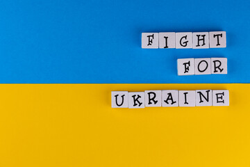 The sentence "Fight for Ukraine" composed of letters on the background of Ukrainian flag. Photo taken under artificial, soft light