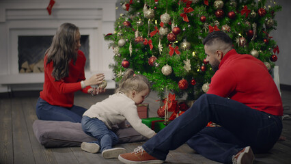 Young parents and little daughter decorate Christmas tree together