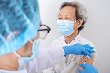 A female doctor is vaccinating an old gray-haired Asian woman wearing a white shirt to build the immune system of the coronavirus, or COVID-19.