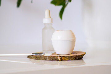 White jar of skin cream and a bottle with a dropper from serum with a brush for applying a face mask. Still life minimalistic beauty cosmetic template. Organic eco friendly products on a wooden plate.