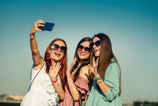Three attractive smiling sisters taking photo on smartphone during walk