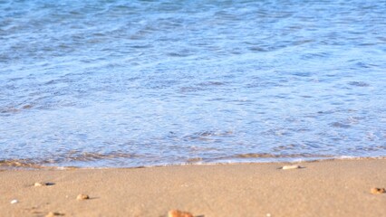 Soft wave of the blue sea on the sandy beach on a summer sunny day.