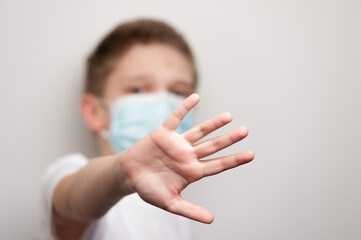 Naklejka premium Caucasian boy in the medical mask and white T-shirt putting his hand forward and stopping something
