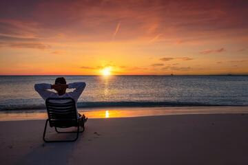 A man on vacation relaxes in a sun chair on a tropical beach during colorful sunset time