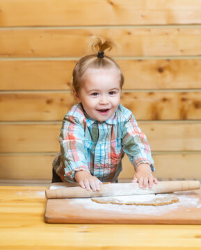 Fun image of baby chef play with flour on wooden kitchen background. Portrait of young kid doing homemade bakery in kitchen. Child sitting on table and enjoy learn to cooking foods or baking.
