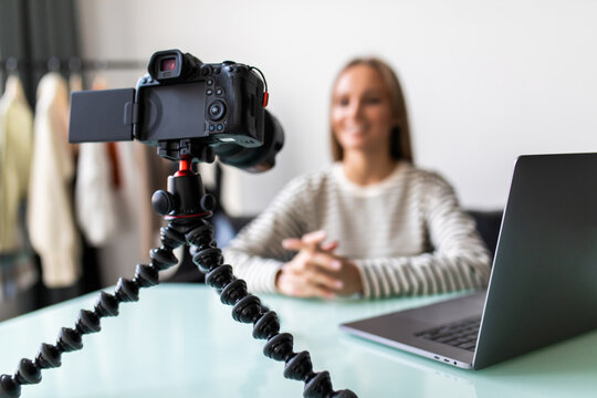 Confident young female vlogger sit at desk shooting live broadcast on professional camera. successful girl speaker or coach talk speak record video tutorial or blog at home