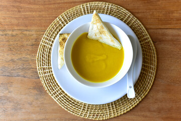 top view of Pumpkin cream soup in a white cup with toast on rustic wooden table. selected focus