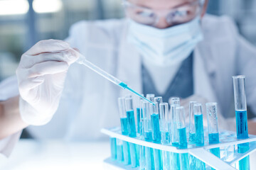 Close-up of researcher using pipette to pour the blue liquid in test tubes at table in laboratory