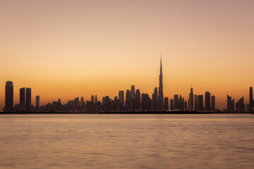 Skyline of Dubai Business Bay with silhouettes of buildings during hazy sunset, orange colors, long...