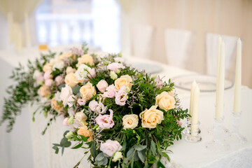 Floral arrangement of white roses on the table in the restaurant next to candles