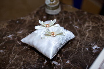 A pillow with wedding rings lies on a marble table