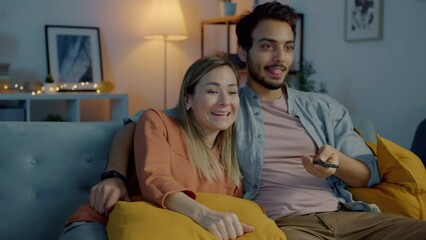 Joyful couple laughing enjoying funny film on TV sitting on couch and hugging in dark living room at night. Happiness and leisure activity concept. - Powered by Adobe