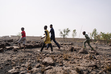 Group of young black African kids crossing a stony infertile field in the Sahel region;...