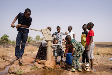 Group of black African school age children gathering around a sub saharian village faucet...