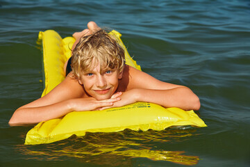 Teen boy swimming on air mattress in the sea and enjoying summer vacation