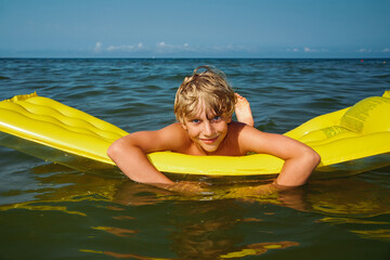 Teen boy swimming on air mattress in the sea and enjoying summer vacation