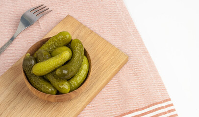 Crispy pickled gherkins in a ceramic bowl with a fork on the table