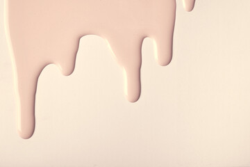 Light brown liquid drops of paint color flow down on beige background. Abstract cream backdrop with...
