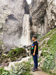 A boy at the Sultan-su waterfall surrounded by the Caucasus Mountains near Elbrus, Jily-su, Russia