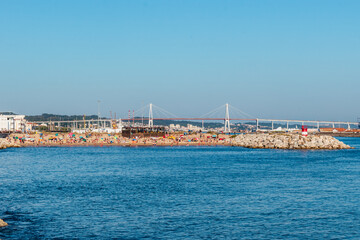 Fototapeta premium Breakwater with a small sandy beach in with silhouettes of holidaymakers and a bridge in the background, Figueira da Foz PORTUGAL