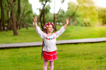 Portrait of  young girl in Ukrainian national clothes on a green background. Outdoors.  Hands outstretched for a hug.