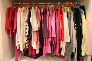 Colorful clothes hanging on a hanger in shop. Clothes hanging on rack in second hand store. Sweaters, shirts, blouses, pants, skirts and other clothes for sale in shopping center.