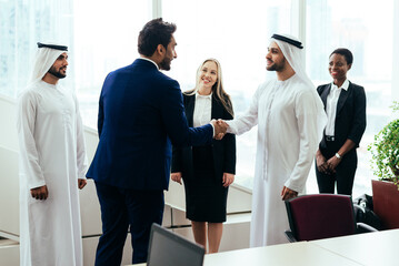 Multiethnic western and middle eastern business team working together in an office of Dubai. Sales people and employees at work on new projects - obrazy, fototapety, plakaty