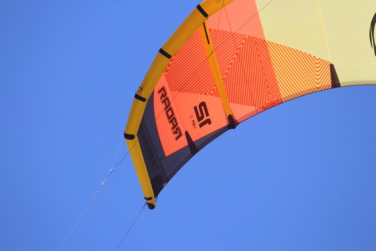 An orange and yellow Cabrinha Radar kite flying in the blue sky. Kiteboarding