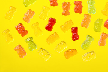 Multicolored flying gummy bears on yellow background, flat lay