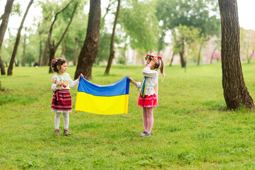 Fototapeta premium Two little girls in national Ukrainian clothes - embroidered shirts, hold the Flag of Ukraine. Glory to Ukraine.