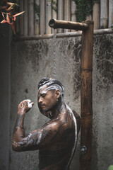 Shirtless muscular latin american male with tattoos standing taking shower outdoors after workout on the tropical leaves background. 