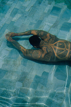 A young handsome mexican man with tattoos is jumping into the pool. A man with a tattoo underwater.