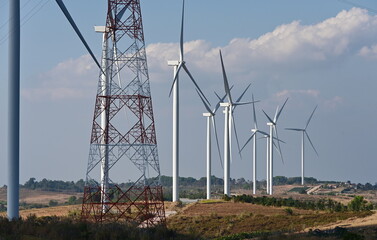 Evening atmosphere of Windmills farm field with white clouds scattered against the blue sky. The electricity energy generating wind turbine along with high voltage electric pole .Use of renewable wind