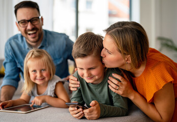 Happy young family having fun time at home. Parents with children using digital device.